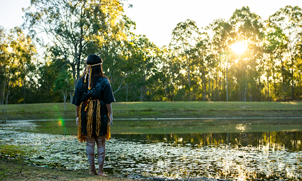 Indigenous girl looking over dam at Hardings Paddock Picnic Area with the sunlight shining through the eucalyptus trees in the backgorund.