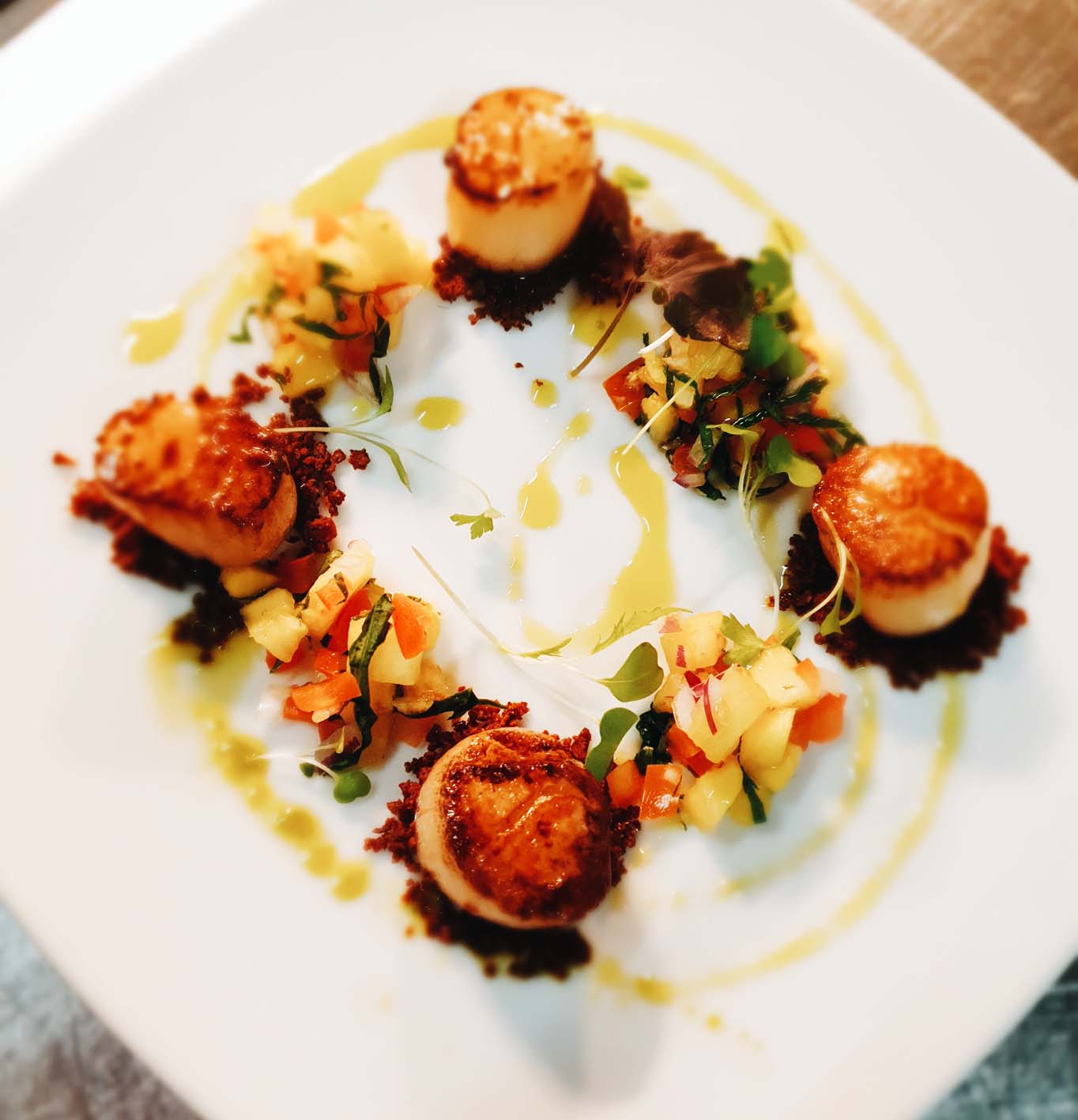 Pan seared Hervey Bay scallops on a bed of chorizo crumb with pineapple salsa and basil oil.