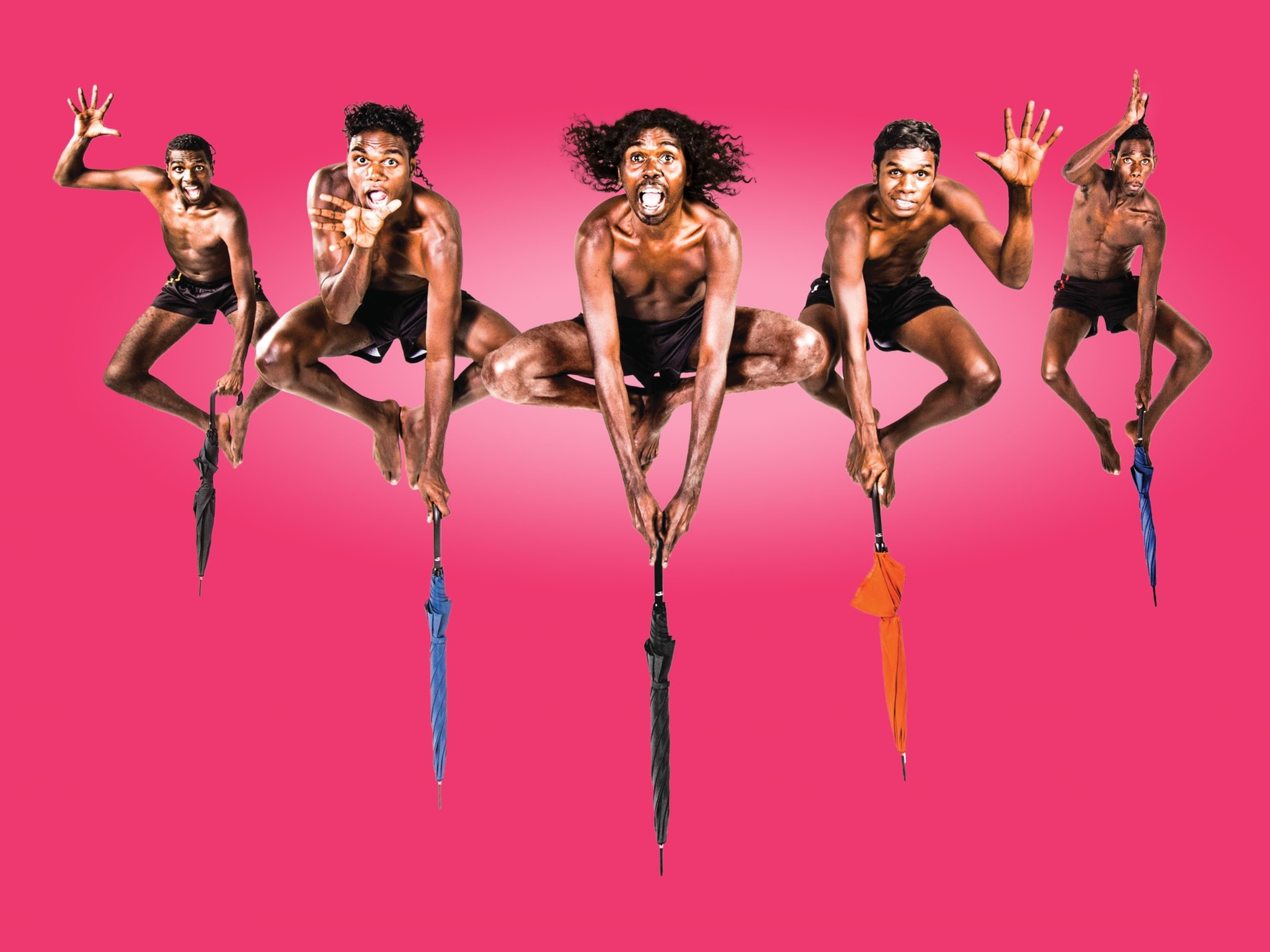 The men of Djuki Mala jumping up on umbrellas posing with bright pink background The men of Djuki Mala jumping up on umbrellas posing with bright pink background