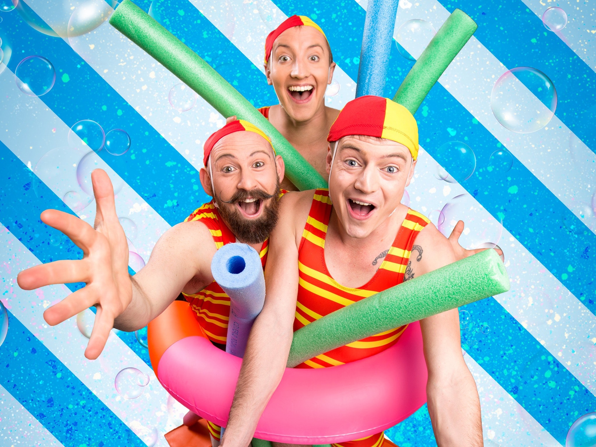 Three men pose in red and yellow swimsuits with pool toys